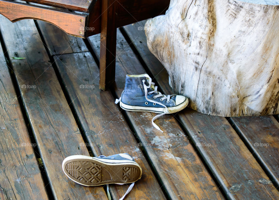 Favorite old shoes high top sneakers on wood deck next to chairs and tree stump vintage table 