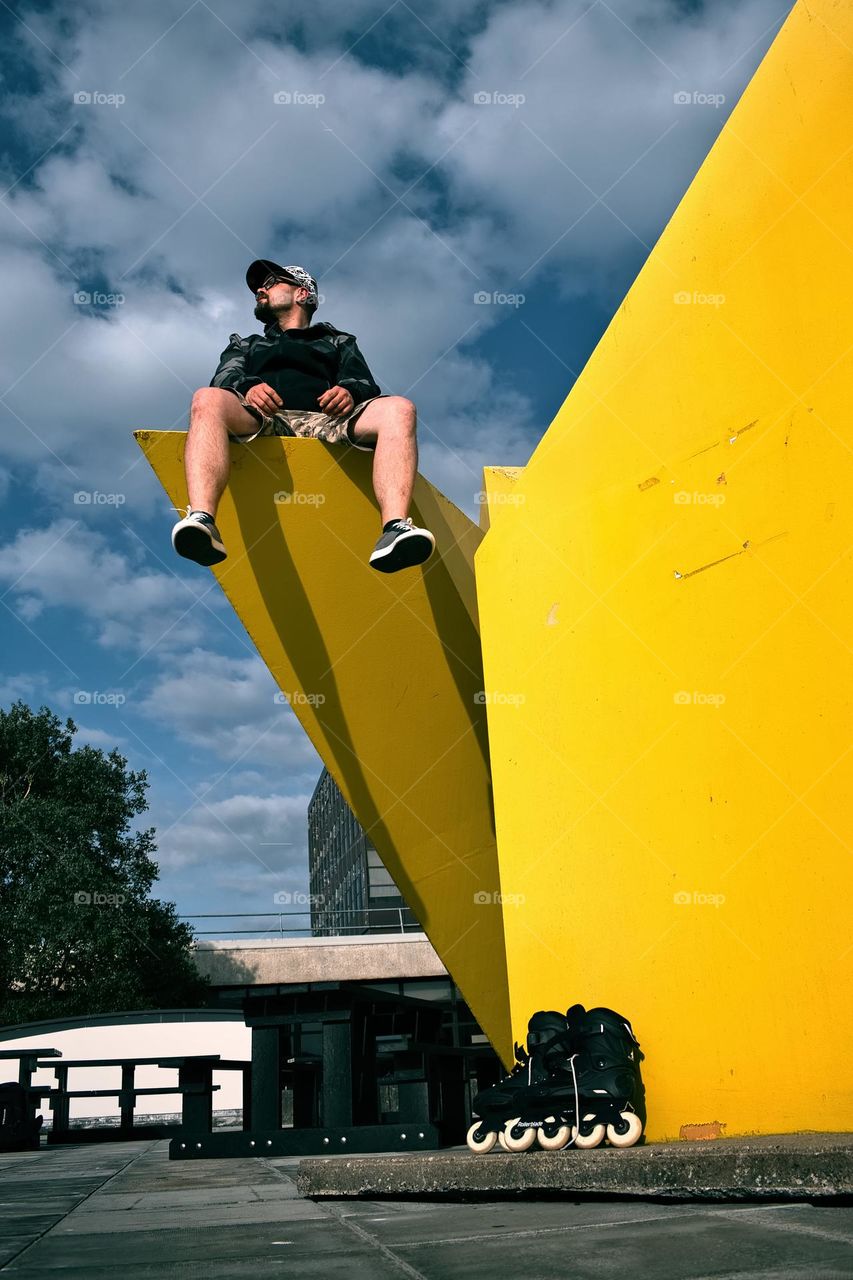 Man sitting on yellow statue with rollerblades underneath