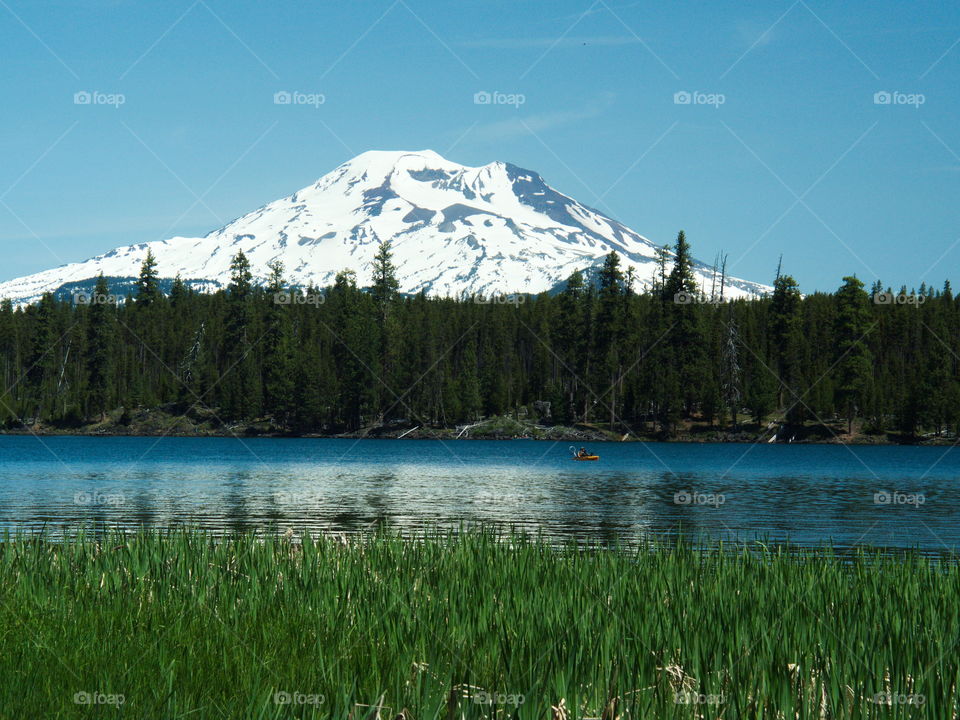 The South Sister with snow behind lava lake on a sunny afternoon with a person kayaking