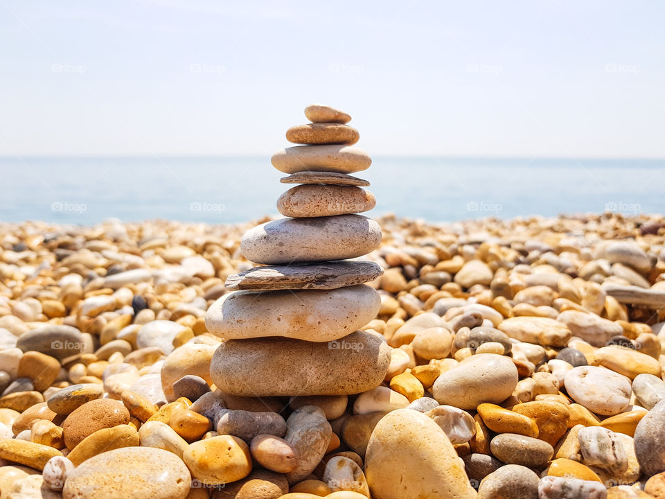 Stone stacking with pebbles around and beach at the background.
