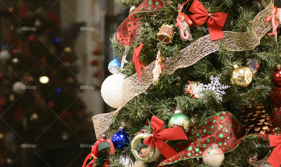 Christmas tree closeup indoors with reflection in window and decoration ornaments of bows and red ribbon 