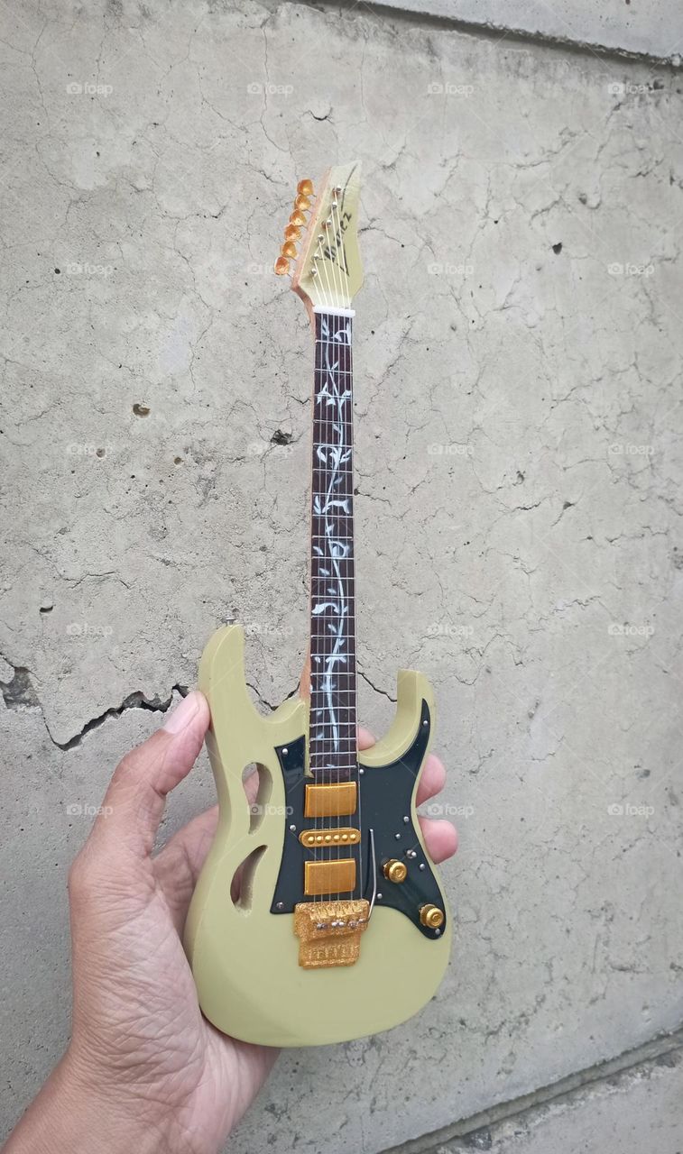 Miniature guitar in a hand with concrete wall as background.