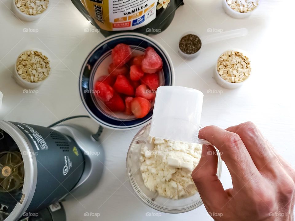 Making a healthy protein shake with oats, chia seeds, frozen strawberries, and protein powder.