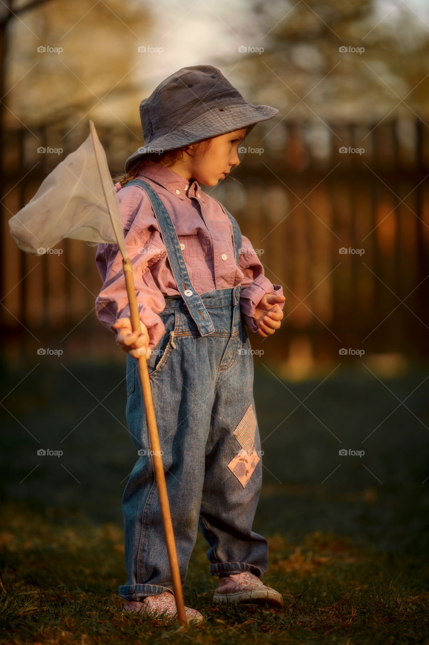 Little girl with butterfly net outdoor at sunset