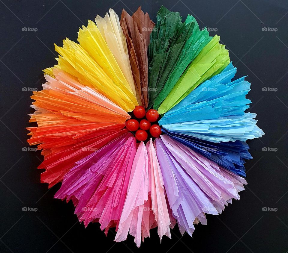 Primary colours flatlay composed of a flower made out of silk papers with cherry tomatoes in the centre on a black background