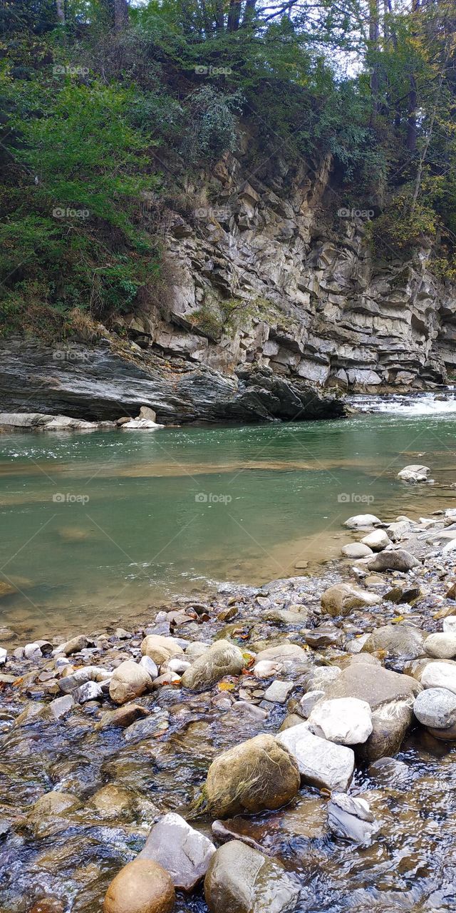 Emerald green water in the mountain river. Stone coast. Beautiful high rock with green trees. Mountain landscape