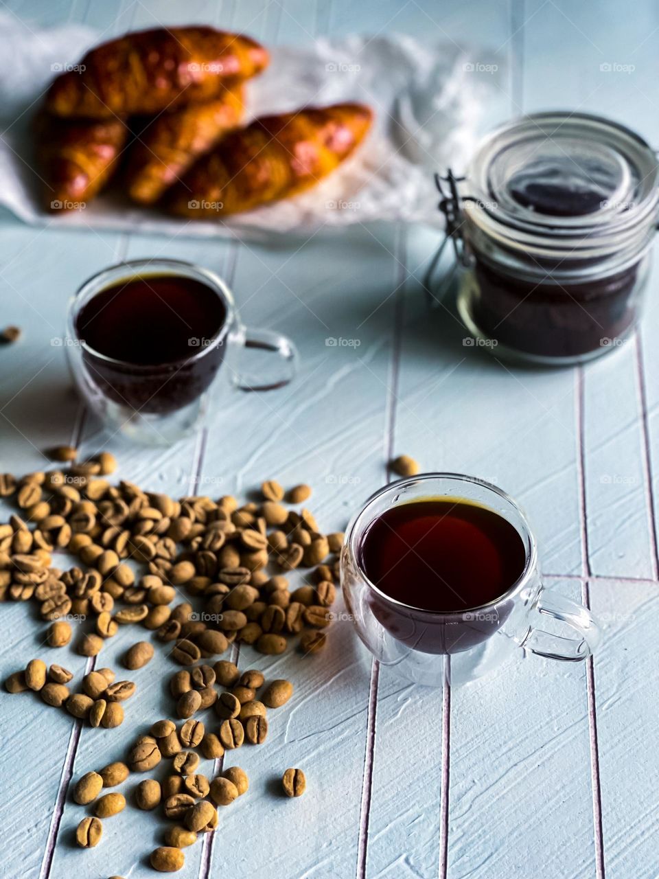 Hot coffee for the winter, croissants at the back and coffee beans scattered at the side