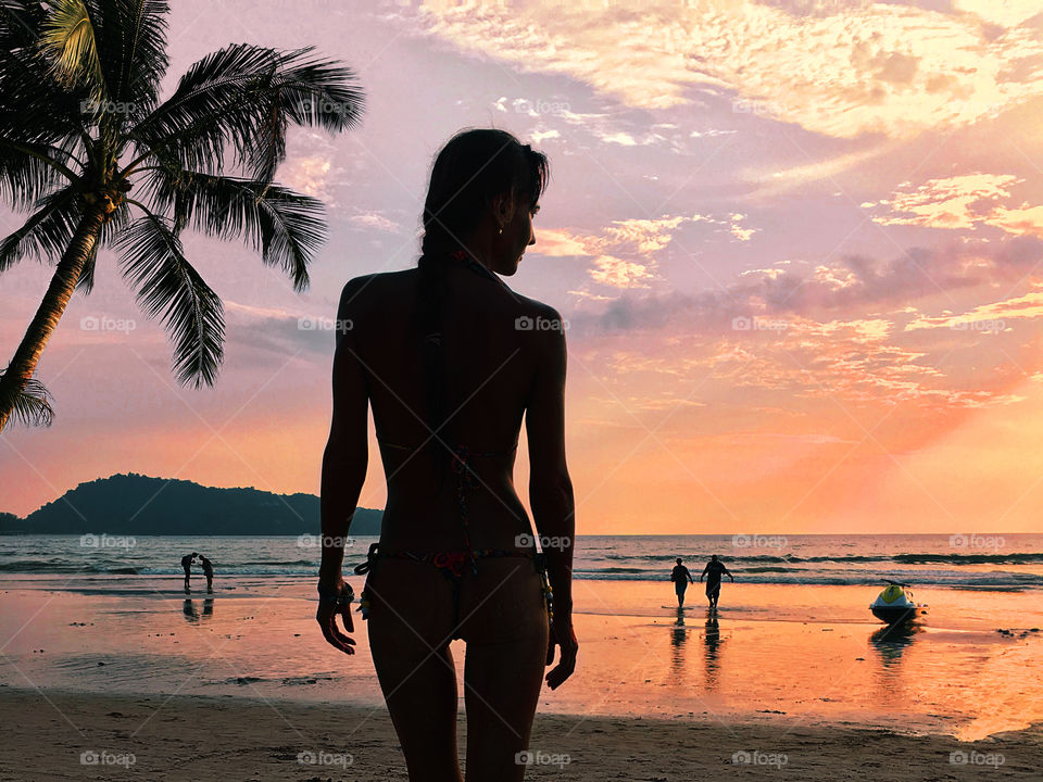 Silhouette of a young woman at the tropical beach with palm trees at sunset 
