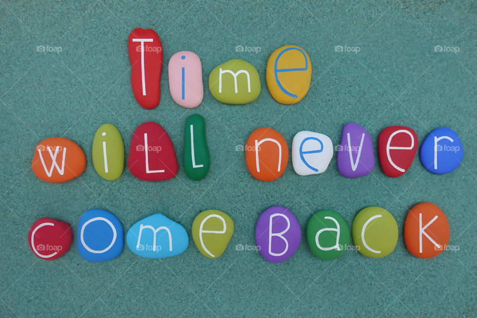 Time will never come back, message composed with colored stones over green sand