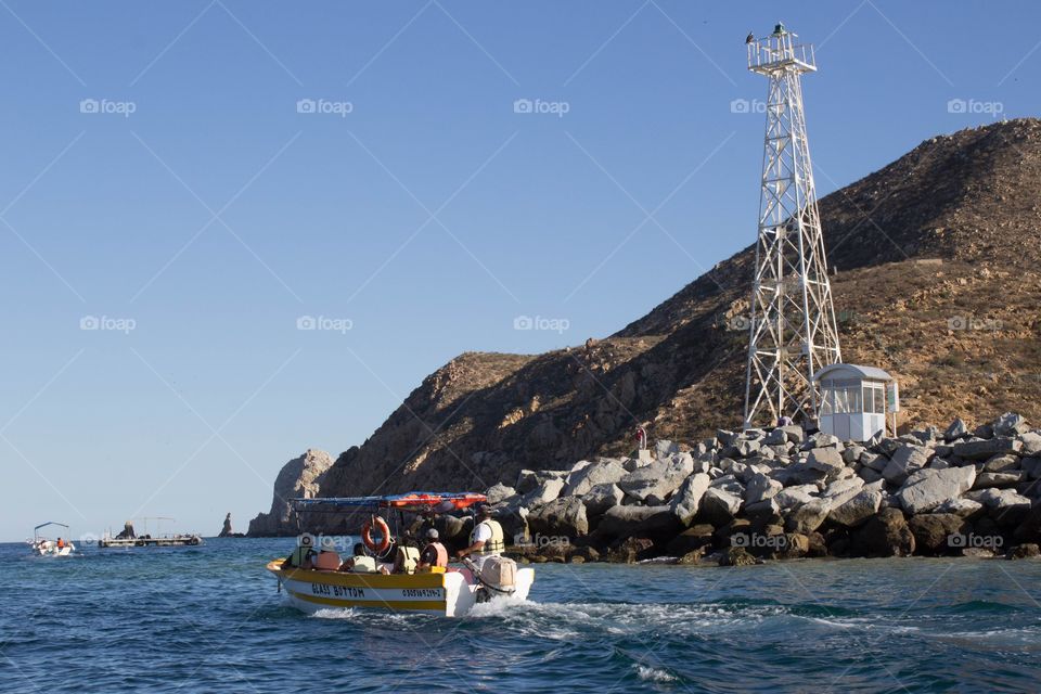 Boat on the ocean with cliffs and a watchtower in the background on a bright, clear sunny day in Cabo San Lucas, Mexico