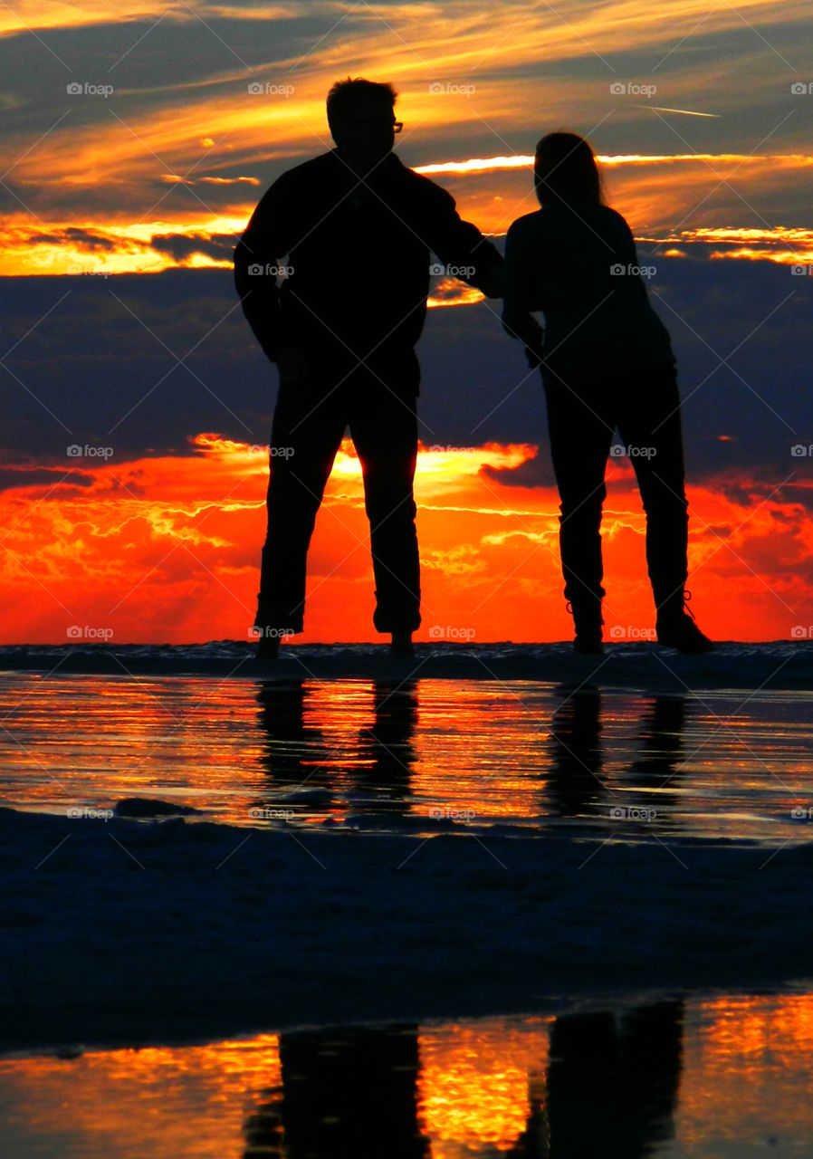 A couple take a romantic walk along the beach in front of the Gulf of Mexico colorful sunset. Sunrises and sunsets of our planet 