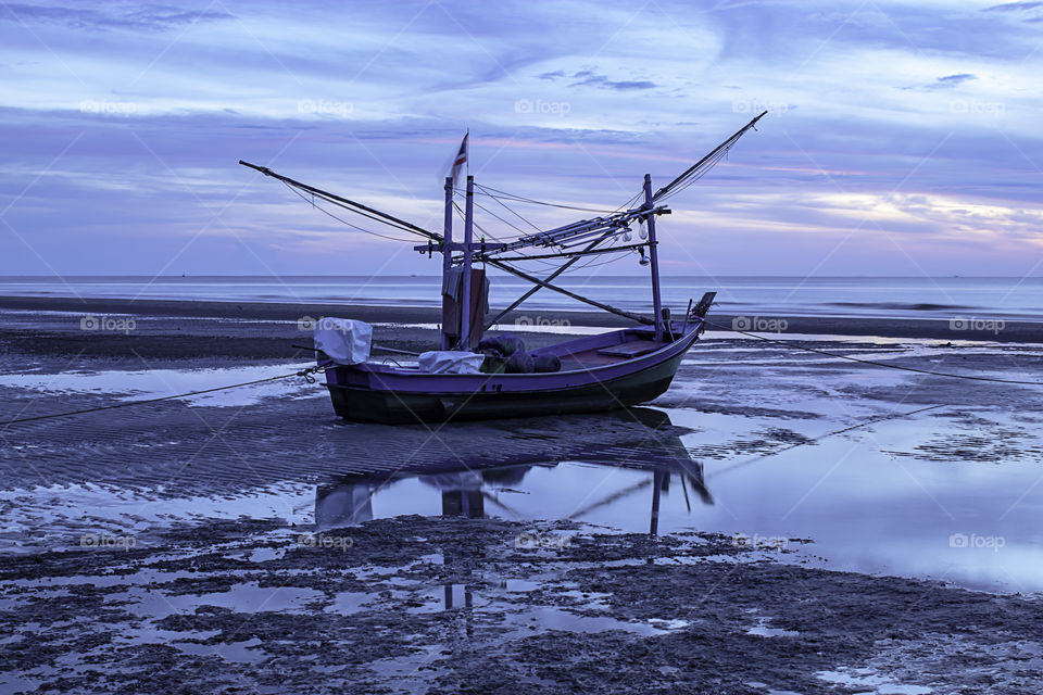 The morning sun light in the sea and the boat on the beach.