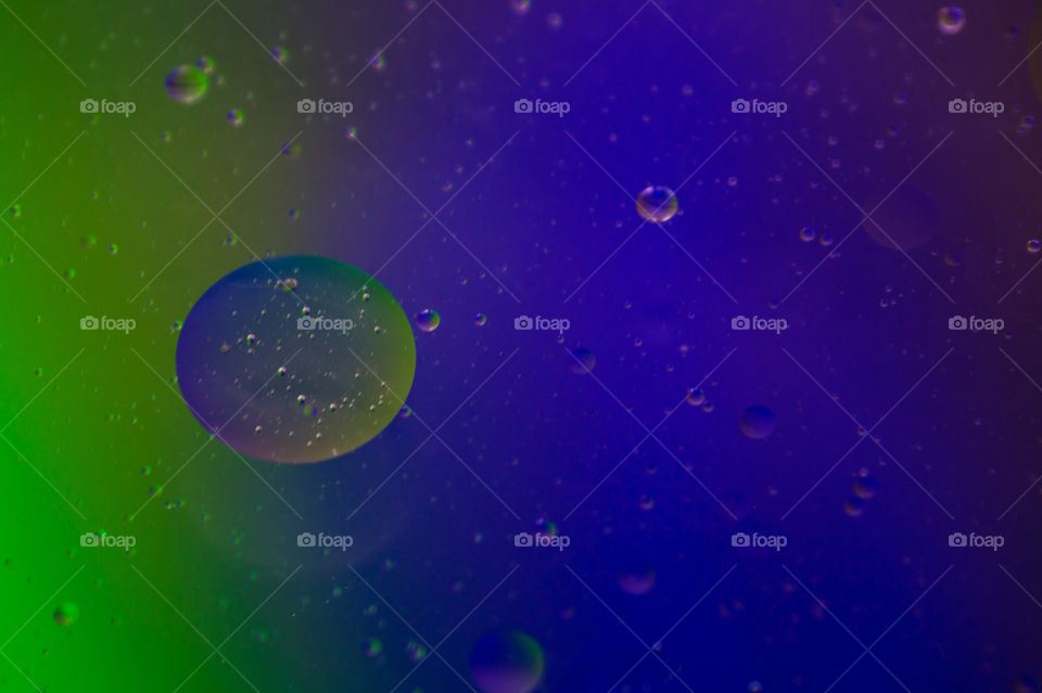 Bubbles of vegetable oil in clear water on a glass and transparent lid from a frying pan on colored paper.