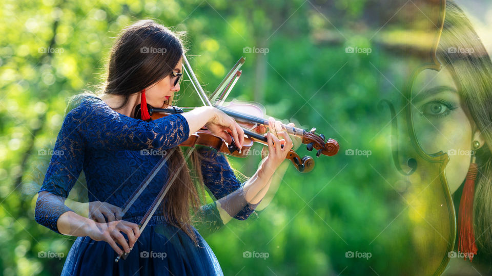 Creative composition. Young woman playing the violin at park. Shallow depth of field.