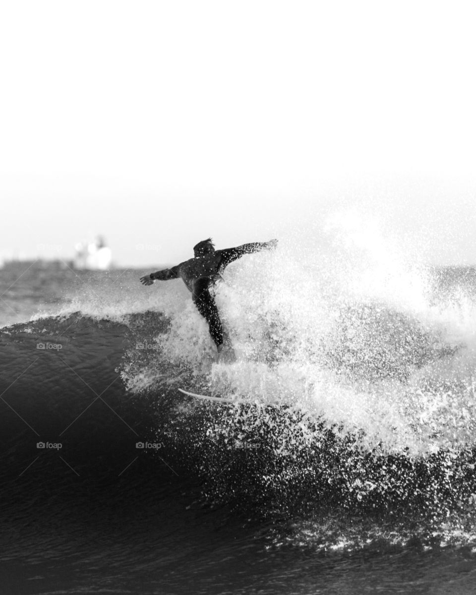 High contrast black and white image of a surfer in a black wetsuit, jumping through the white wave break. 