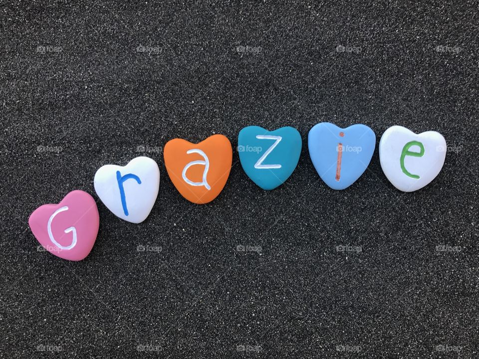 Grazie, italian thank you with colored heart stones over black volcanic sand