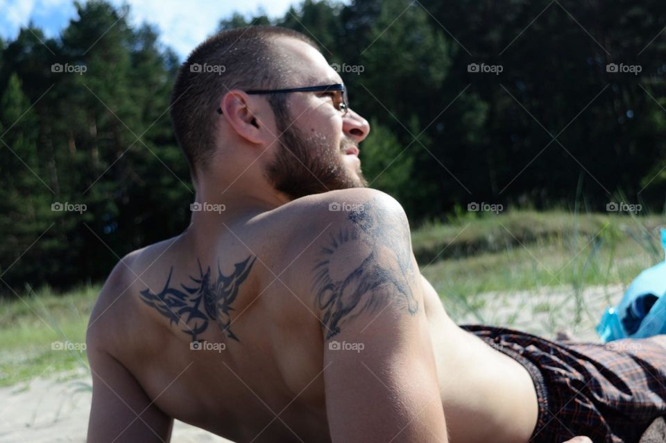 Men with tattos lying on the beach and engoying hot summer day