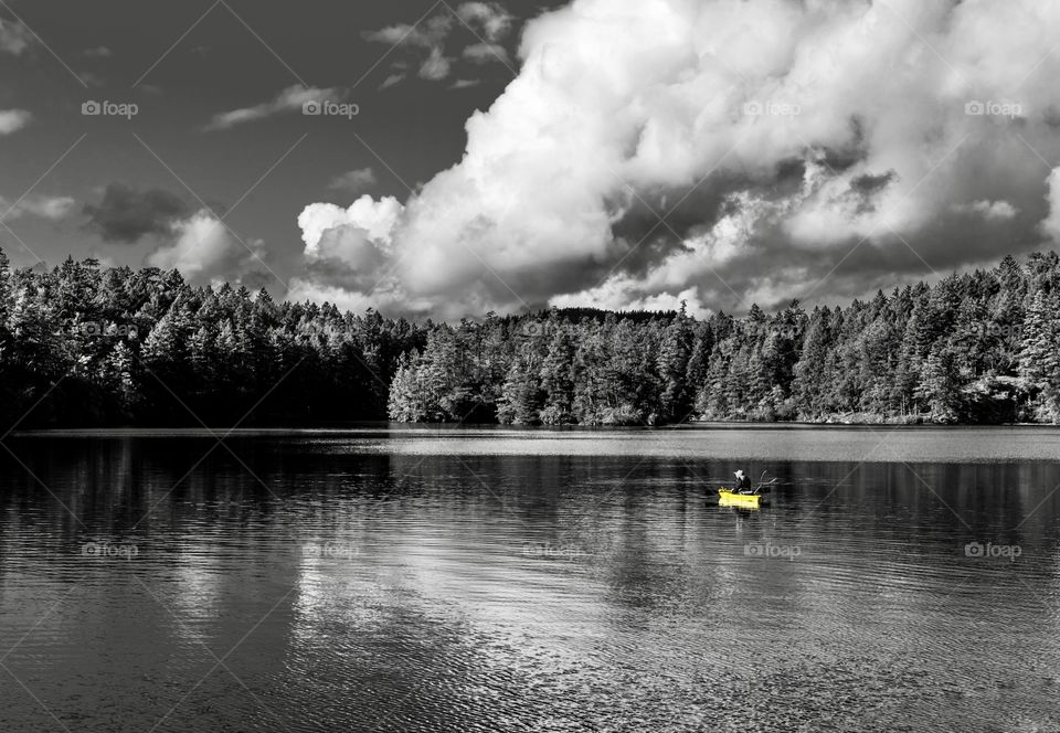 Half white, half black sky and lake with a fisherman on a bright yellow boat 