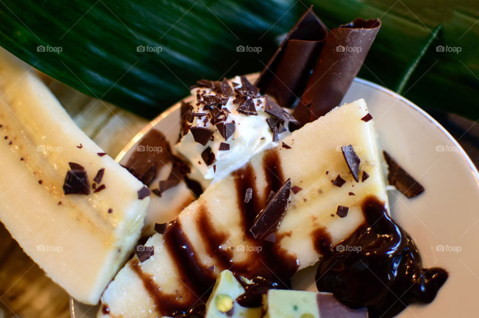 Chocolate fudge banana split on plate with dark chocolate sauce, pieces on fudge and whipped cream with chocolate sprinkles - different kinds of chocolate garnish from high angle view photography 