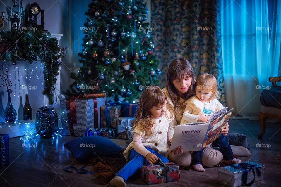 Little sisters with mother reading the book at Christmas Eve 