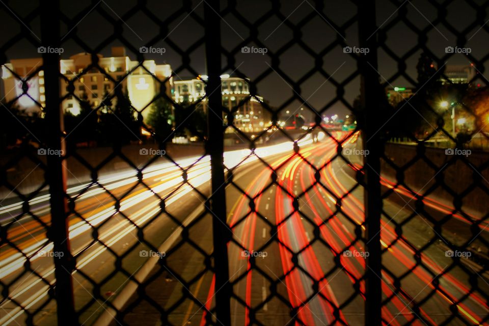 standing on an overpass overlooking the freeway taking a long exposure photograph of cars going by.