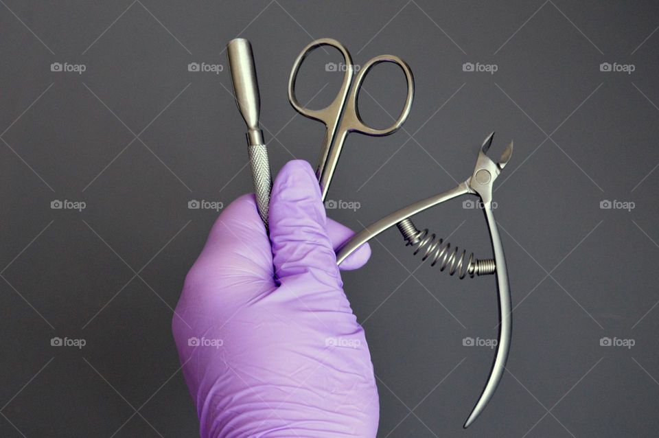 Manicure tools are held by a manicurist in rubber gloves