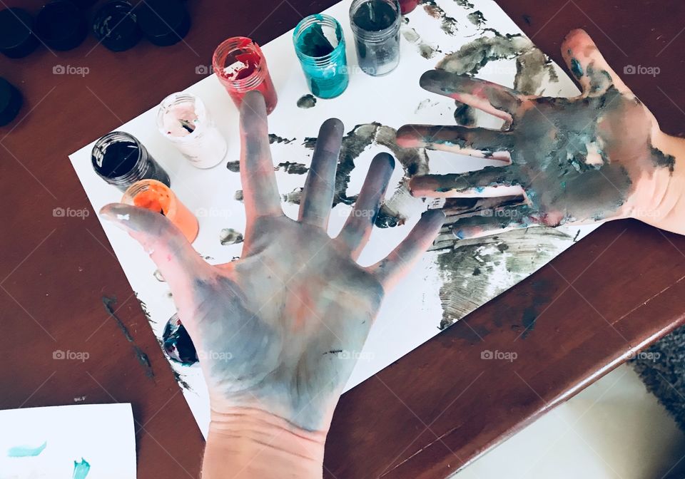 School art project using paint - mother and son showing messy hands and hand prints after creating a picture with brightly colored finger paints