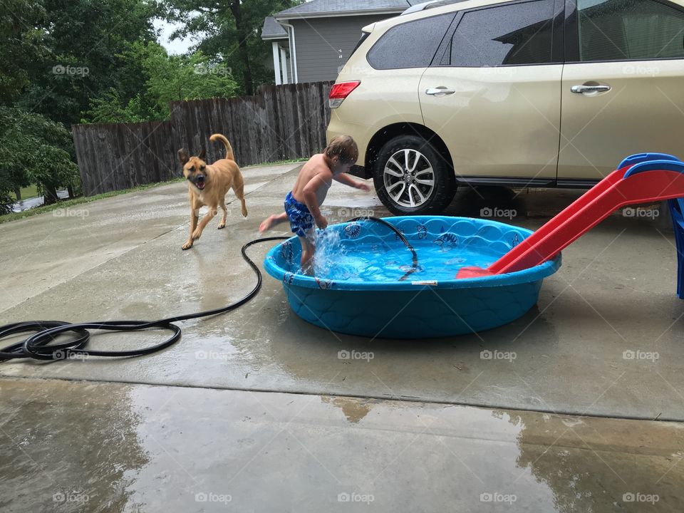 Little boy playing in kiddie pool with dog by his side