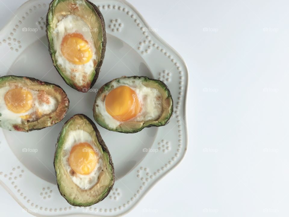 Breakfast Time Shots - flat lay of eggs baked in avocado halves on white plate, white background 