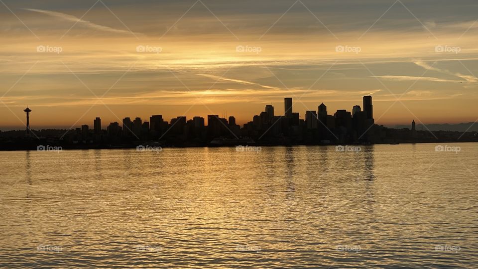 Silhouette photo of Seattle skyline during morning golden hour taken from the Bainbridge Island to Seattle Ferry, September, 2021. Space Needle far left and the old Smith Tower on the far right of photo. Puget Sound foreground.