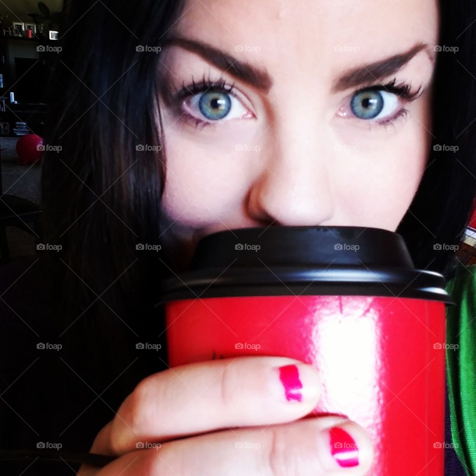 Young woman with blue eyes drinking from a red and black coffee cup.