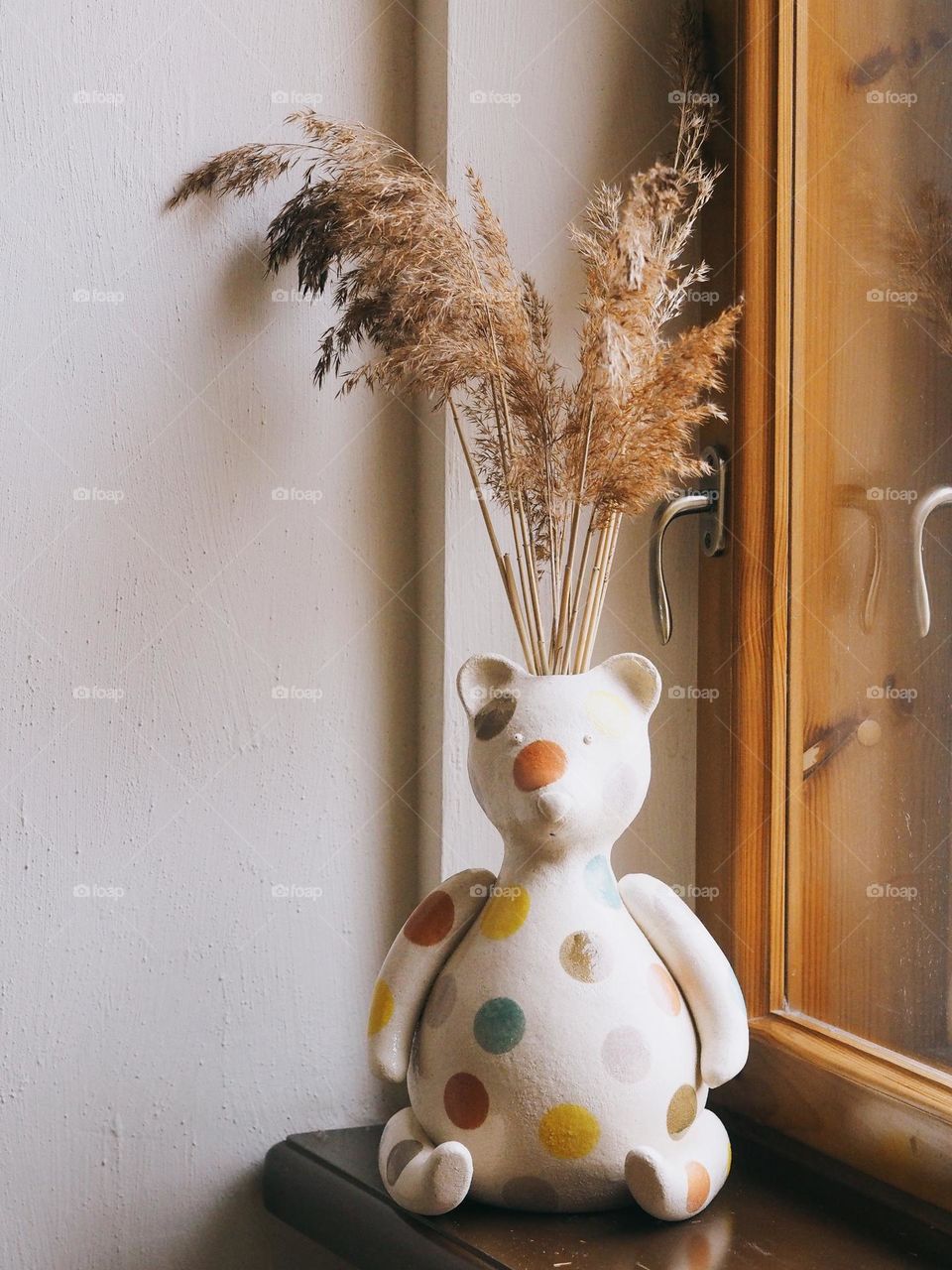 Dried flowers in general in the shape of a bear on a wooden windowsill near the window.