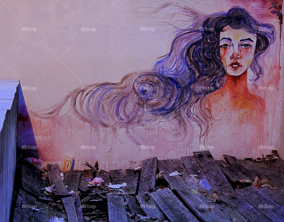 A painting on a back alley. Broke  wood pieces and trash at the bottom. A contrast of human beauty and waste.