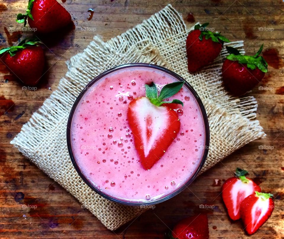 Strawberry banana smoothie sitting on burlap napkin with fresh strawberries on wood table