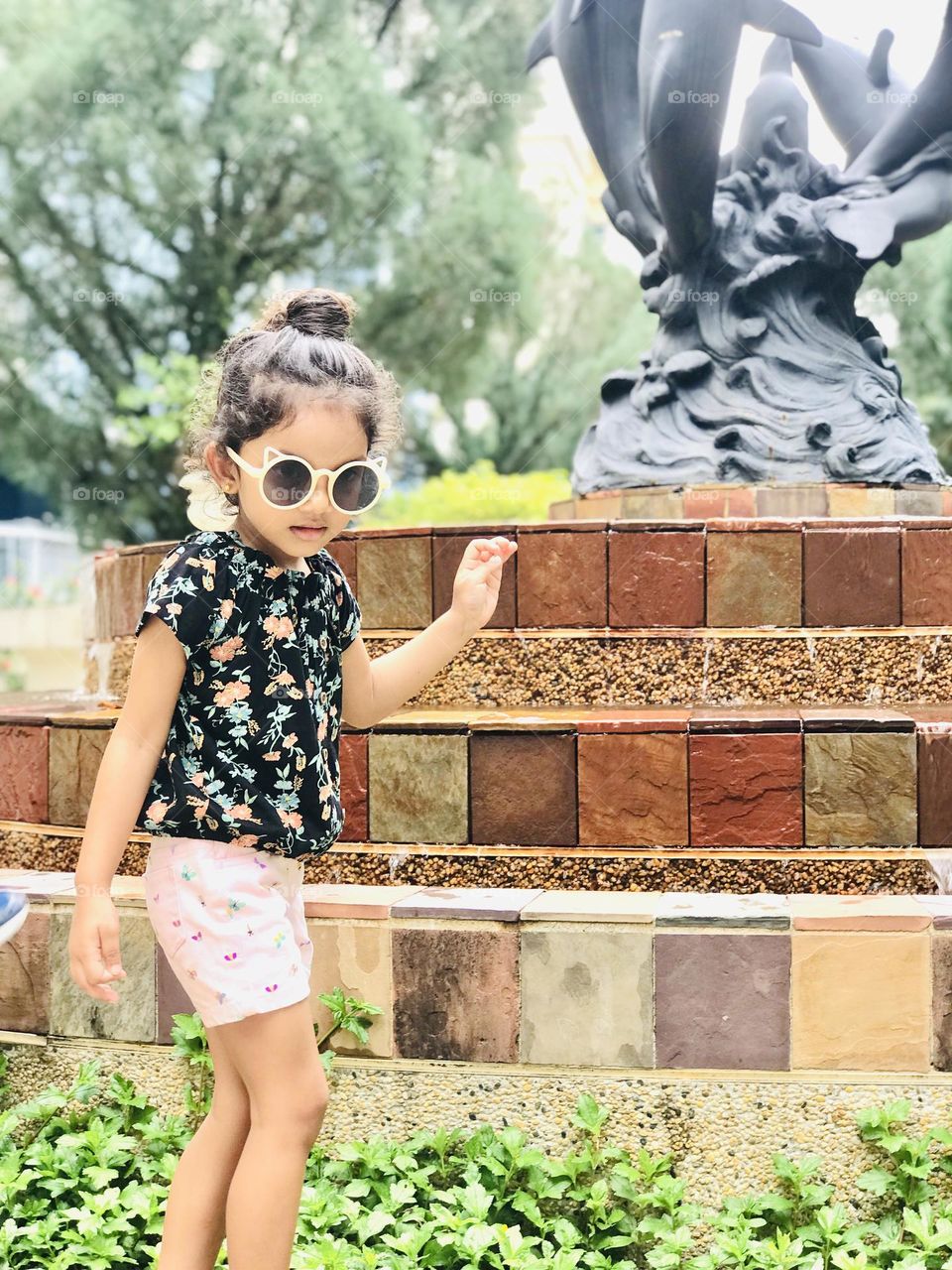 A Cute little Girl girl cute giwearing summer outfits and she is playing with water.