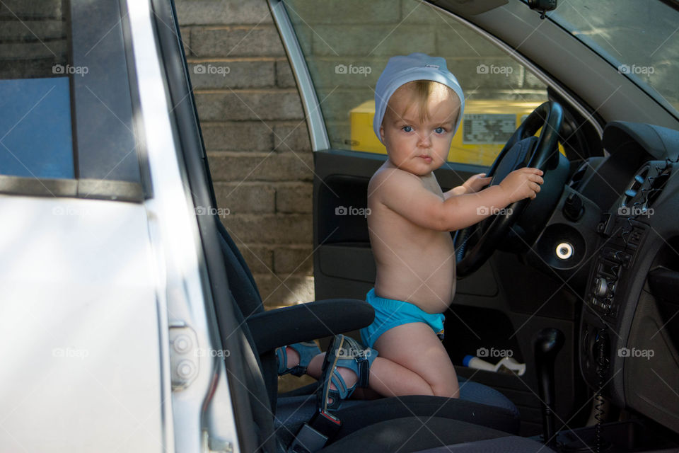 Shirtless boy sitting in car holding steering