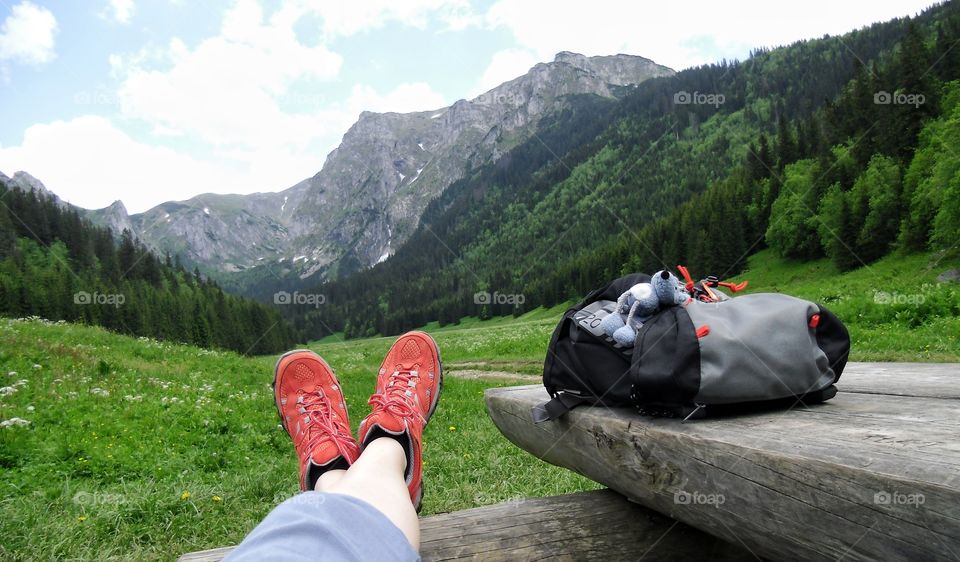 A man laying outdoors on a wooden park bench, relaxing and enjoying a view of the mountains