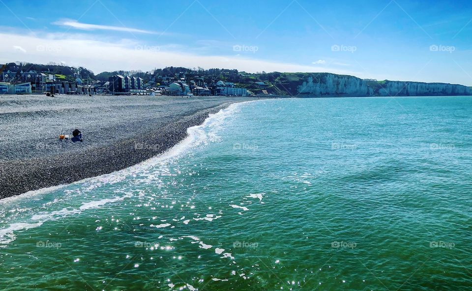 Blue sea, white cliffs and pebble beach of Fécamp, Normandy,France under a clear blue sky