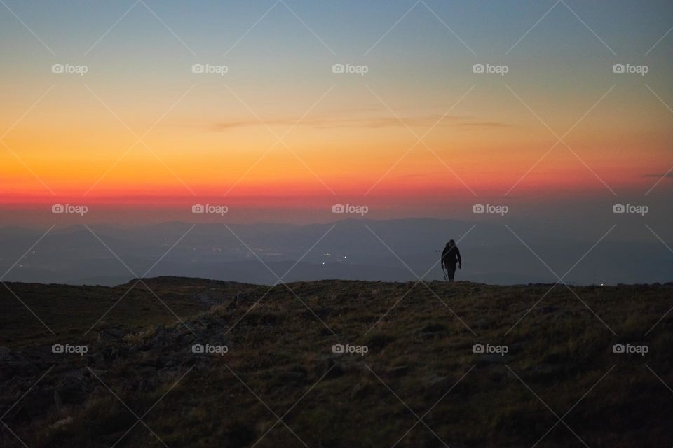 Man looking at sunrise. Mountains at sunrise. Man standing on peak. Natural mountain landscape with illuminated misty peaks, foggy slopes and valleys, blue sky with orange yellow sunlight. Amazing scene from Beskid Zywiecki in Poland