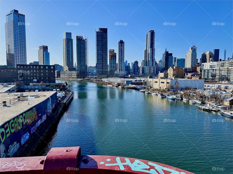 This is beautiful „Newtown Creek“ seen from the „Pulaski Bridge“ that connects „Greenpoint“, Brooklyn to LIC, Queens. Across the water of the „East River“ you see LIC and in the furthest distance „Manhattan“. 2024. Hypnotic Productions
