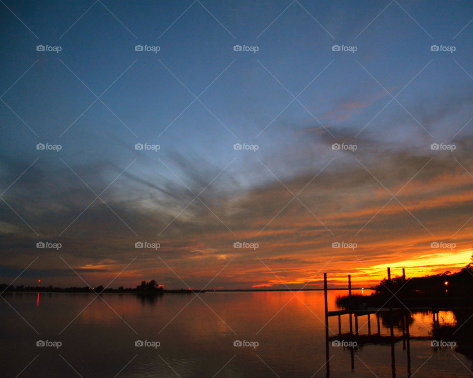 The clouds in the sky are illuminated by rays from the brilliant golden sunset! The sunset also reflects off the shimmering bay water!