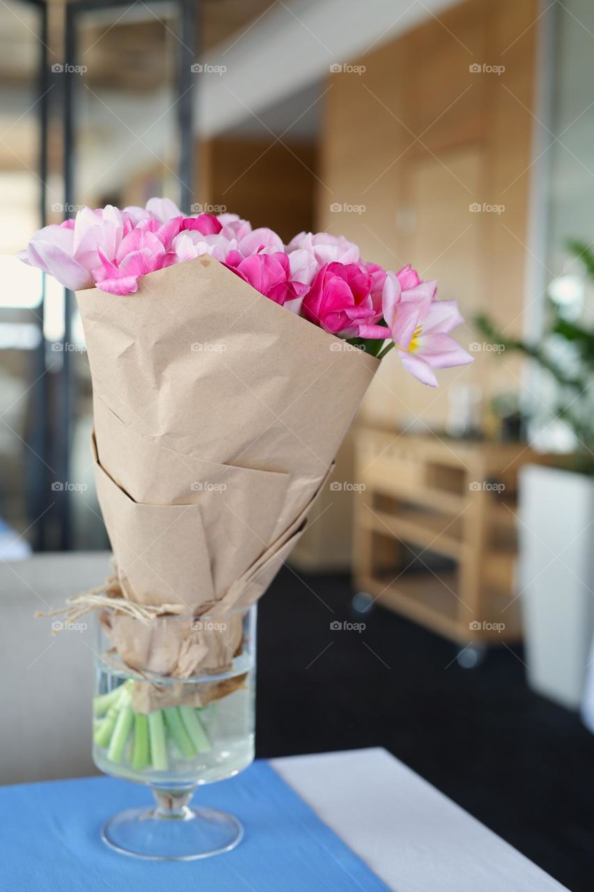 a beautiful vase is on the table, and in it are tulips in craft paper