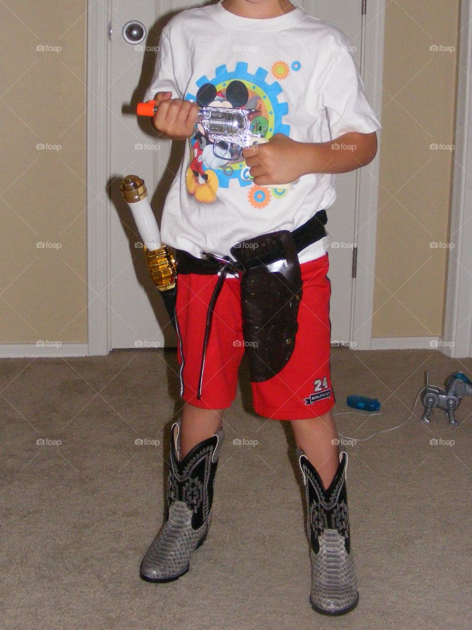 This boy is wearing cowboy boots. He is holding a toy gun and wearing a gun holster.