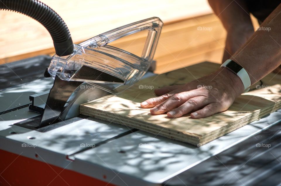 A male carpenter saws chipboard and a wooden board with circular saw on the machine