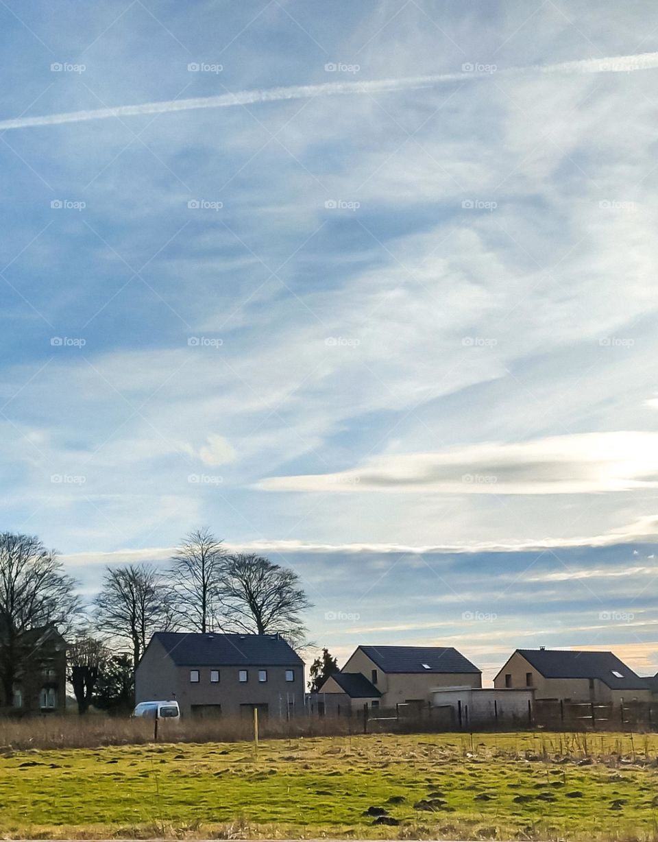 Beautiful view of a rural landscape with a field, houses and a clear cloudy sky in Belgium, close-up side view.