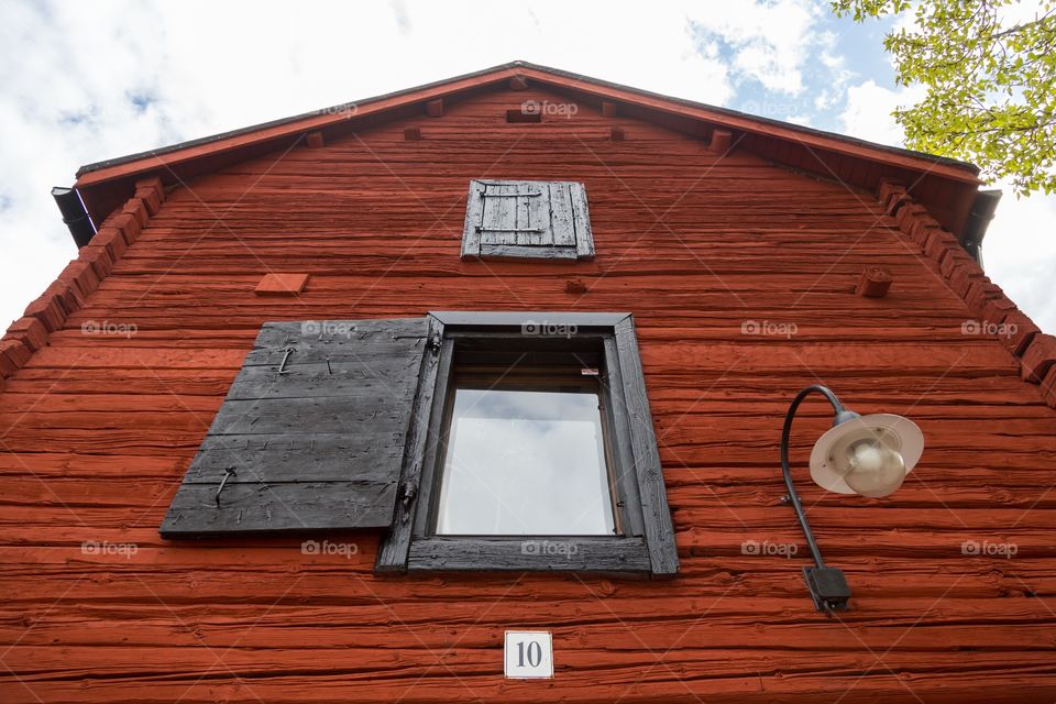 Old red wooden house. Old red wooden house against partly cloudy blue sky. Two windows, one closed with wooden cover. Black streetlight