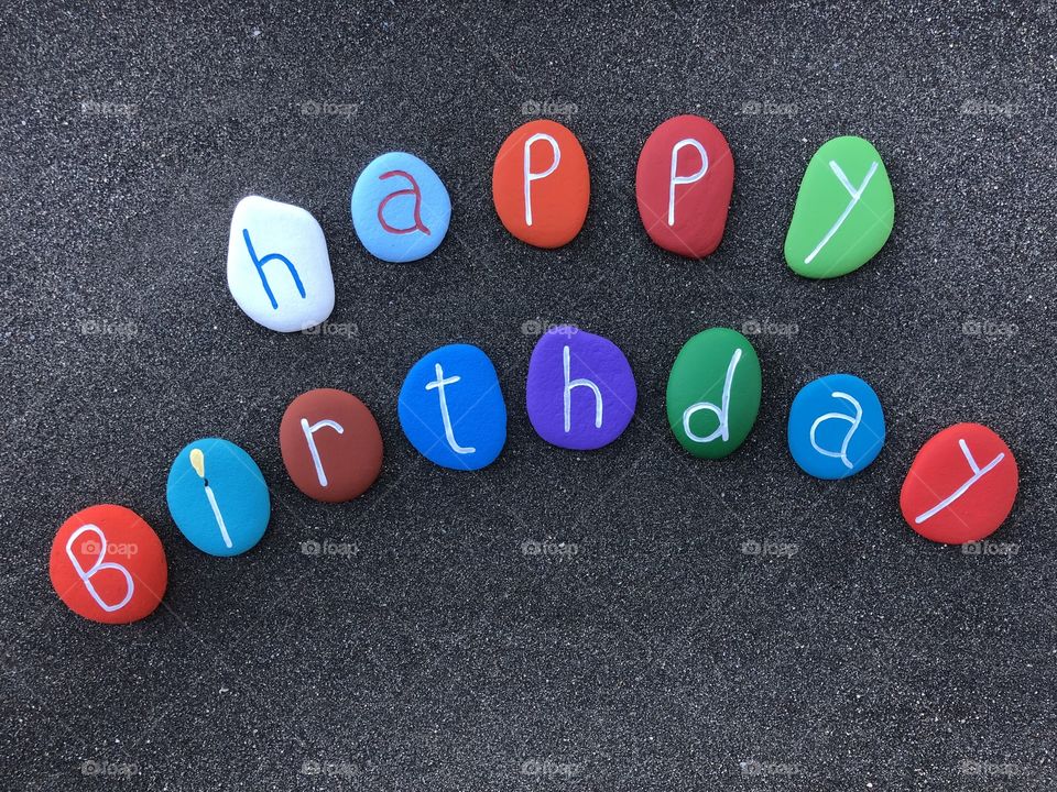 Happy Birthday text with multicolored stones over black volcanic sand