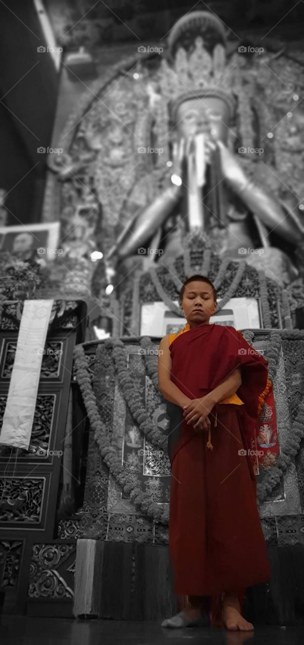 A little Buddhist monk stands in front of statue in a temple in Nepal