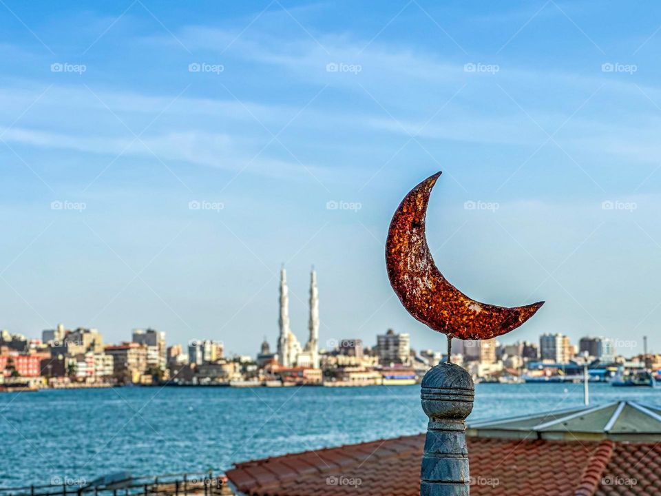 A crescent ornament with a mosque in the background and the Suez Canal in between.