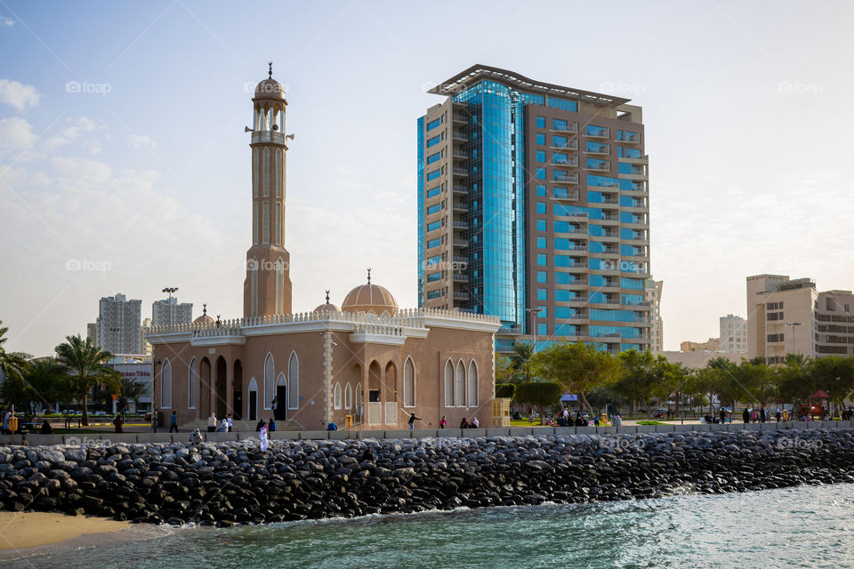 a mosque on the edge of he sea with a modern building behind